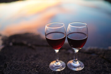 Close up on hands holding red wine glasses on the beach during sunset, celebration concept
