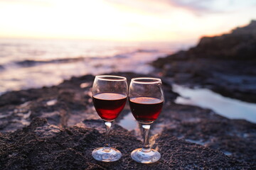 Close up on hands holding red wine glasses on the beach during sunset, celebration concept