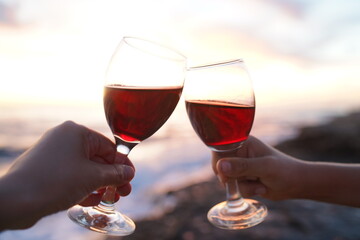 Close up on hands holding red wine glasses on the beach during sunset, celebration concept