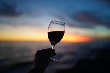 Close up on hands holding red wine glasses on the beach during sunset, celebration concept