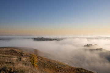 Autumn landscape in the early morning. Fog-covered expanses through which the first rays of the rising sun pass. Trees and hills in the fog. Dawn on a cold autumn morning.
