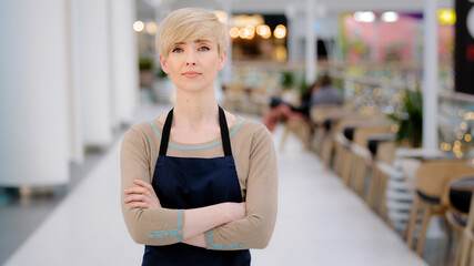 Mature adult middle aged 40s woman lady restaurant cafe worker looking at camera posing crossing arms female waitress saleswoman in apron standing at work space profession concept. Small business