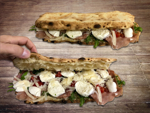 Neapolitan Panuozzo, with fresh and raw ingredients, mozzarella, tomato, ham, rocket and flaked parmisan. Italian food.