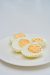 Boiled eggs on a kitchen table, healthy breakfast and protein rich diet. Eggs on a plate with a knife on a side, airy and white background with green plants and a light reflection from the table.