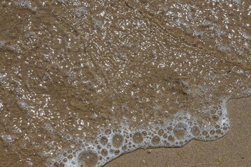 Close-up of sea foam on the sand beach with summer sunlight