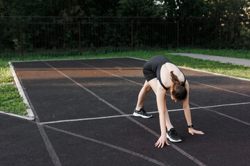 A fitness woman doing a stretching exercise stretches her legs. Women stretch to warm up before running or training. In the park, on the sports field. side view, yoga elements.