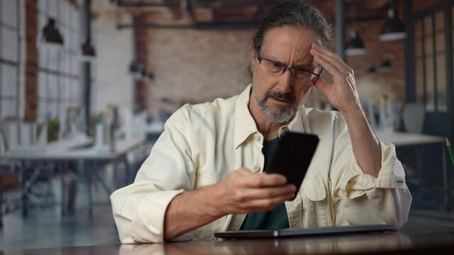 Mad unhappy man feeling annoyed using smart phone. Angry businessman having problem with mobile spam message. Male user frustrated by low battery or bad signal concept sitting at office desk.
