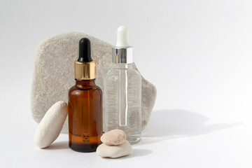 Multi-colored stones with a transparent bottle with a pipette on a white background. Natural podium with cosmetics