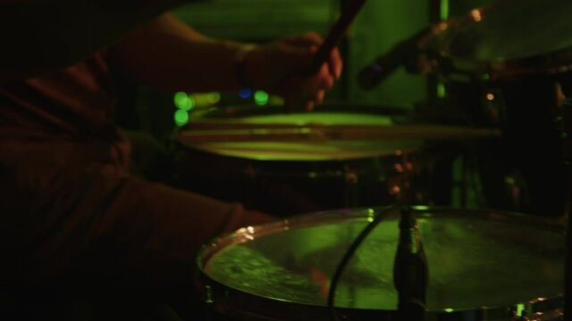 Drummer hits on the drums with mallets drumsticks. Young man playing drums on stage. Drums and cymbals during playing. Drum set, drum kit in dark, drummer plays a concert. Concert. Neon light