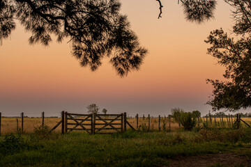 Atardecer en el campo con tranquera en primer plano