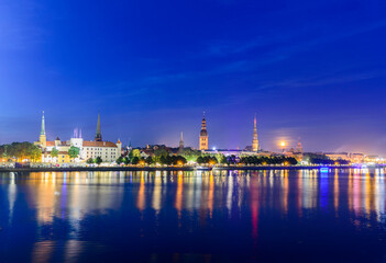 Obraz premium Old Riga and Daugava river at Ligo (Saint John) night. Dark blue night sky, full moon, illuminated medieval castle and old town churches