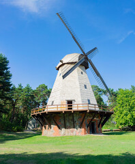 Fototapeta na wymiar An old european wooden windmill on stone and brick basement, blue sky, green trees and grass