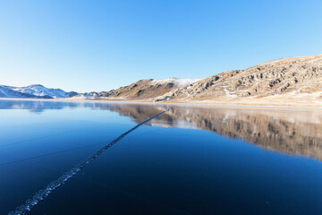 Obraz premium Beautiful winter landscape of frozen Lake Baikal during freezing in the bays. Snow-covered coastal hills are reflected in the expanse of blue ice at sunset. Winter outdoor recreation and ice travel