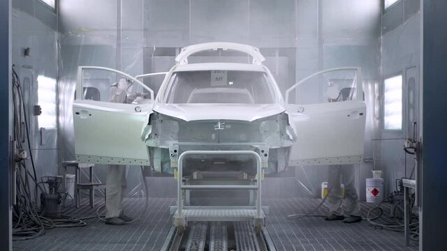 Two men paint a car in a spray booth. Car manufacturing.