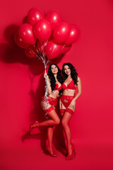 Obraz na płótnie Canvas Vertical full length body size view of two cheerful gorgeous girls holding festal balls having fun isolated over vivid red color background