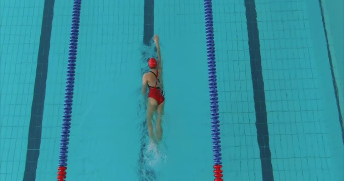 Young female athlete is rowing with her hands, swimming in a crawl style. Female swimmer trains in the pool, blue water. Woman swims in protective glasses, a swimsuit and a hat. 4k, ProRes