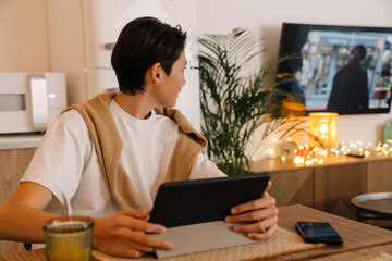 Asian boy using tablet computer while watching tv in kitchen