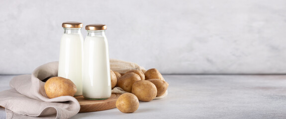Vegan plant based milk in two glass bottles. Alternative potato milk and potato tubers on gray table