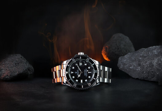 The Rolex vintage wristwatch ceramic bezel model black oyster perpetual submariner date 39 mm display on black table with background of flame and rocks in the dark shelf of luxury watch exhibition