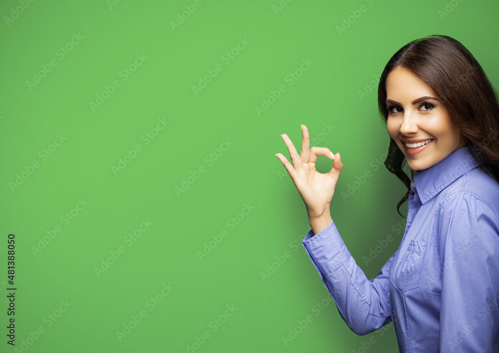 Canvas Prints Portrait image of happy smiling showing okay ok hand sign gesture businesswoman, isolated on green color background, with copyspace. Young cheerful brunette woman in blue cloth at studio ad concept.