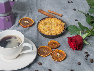 Coffee pot with coffee beans, dried oranges, apple pie, cinnamon stick and red rose on a brown background..