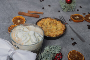 Cup with coffee and cream and apple pie, coffee beans, dried oranges, sprig of spruce on and christmas decorations on brown background.