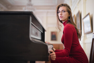 Fototapeta na wymiar Young girl in the red dress sits by the piano.
