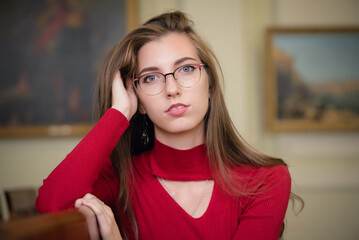 Young girl in the glasses and red dress in the art gallery close up portrait.
