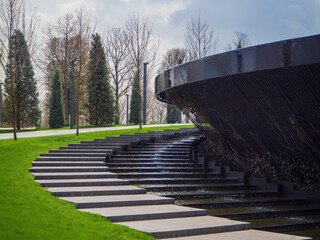 Dry and wet steps in the park near an artificial waterfall flowing from a round fountain bowl....