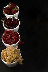 Blurred image of various fruits and berries in white plates on a black background with space for text input.