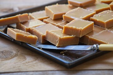 Homemade fudge squares on a baking sheet in warm sunlight on an old wooden table