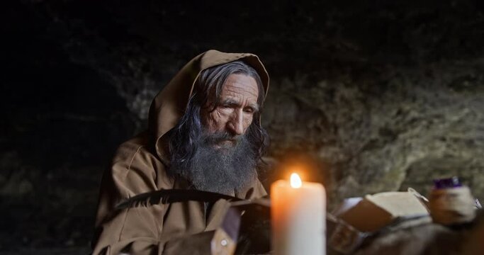 Aged hermit writing book in cave