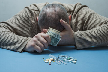 The man hides his face with one hand, holds money in the other, medical preparations are on the...