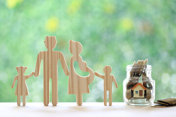 Happy family with model house and gold coin money in the glass bottle on natural green background,...