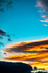 Fototapeta na wymiar A portrait image of golden orange and yellow clouds against blue skies during sunset across the Mediterranean coastline on Marbella 