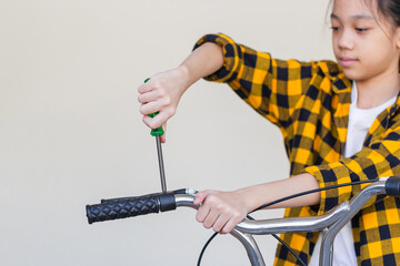 Kid girl repairing her bicycle at garage, little girl using a screwdriver fixing bike, hobby and repair concepts