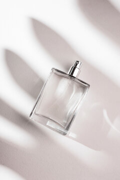 Transparent bottle of perfume on a white background. Fragrance presentation with daylight. Trending concept in natural materials with palm leaves shadow. Women's and men's essence.
