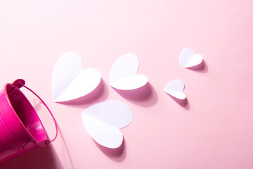 Valentine's Day background. White volumetric paper hearts and pink bucket on a nude pink background. Valentine's Day concept
