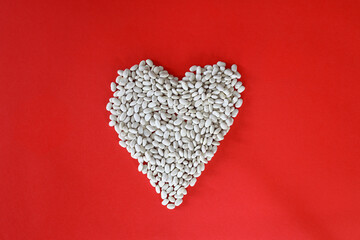 A pile of Dried white Kidney Beans in the shape of a heart on the red background. Healthy food concept. love food, heart food, valentine\'s Day concept. Flat lay, copy space
