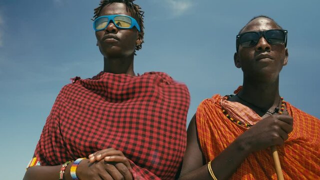 Epic Style Dolly Shot of Two Young Masai Tribe Members in Traditional Red Dresses and Sunglasses Standing on the Sand Beach of the Indian Ocean. Zanzibar. Tanzania. 4K 50fps