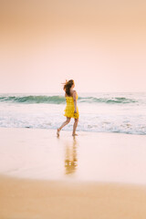 Goa, India. Young Caucasian Woman In Yellow Dress Enjoying Life And Running Towards Sea Waves