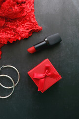 Small red giftbox, red lipstick, silver earrings and lace underpants. Valentine's Day objects on dark background. Flat lay.