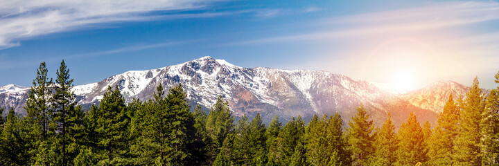 Fototapeta na wymiar Panoramic landscape scene with sun shining behind the snow capped mountains in Lake Tahoe California