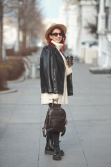 Full length urban fashion portrait of stylish millennial woman in modern clothes walking on city street