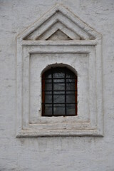 Fototapeta na wymiar Window in an old building. White wall with a window and carved stone architraves.
