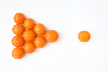 Yellow tomatoes are stacked on a white table in the form of an arrow and next to one yellow tomato