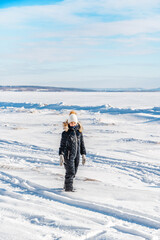 A happy little girl alone in the middle of a snowy desert on a frozen river on a sunny winter day