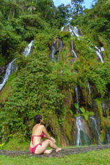 Rear view of unrecognizable woman in swimsuit at thermal springs in Colombia. Vertical panoramic view of woman sit in jungle waterfalls in Santa Rosa Cabal. Colombia travel destination