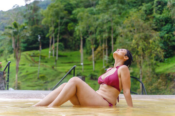 Horizontal view of latin american woman wearing pink bikini at thermal springs in Colombia. Full length view of woman bathing at hot baths in Santa Rosa de Cabal. Travel and relax concept.