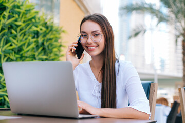 Young beautiful woman in eyeglasses working on laptop and sitting in cafe outdoors People and technology. Lifestyle concept